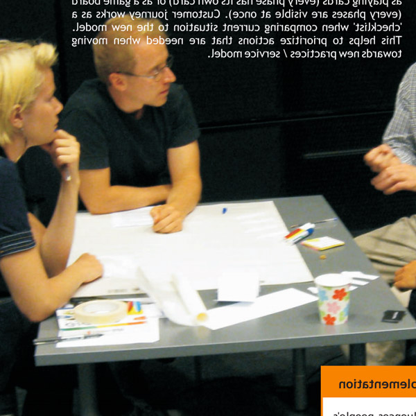 Photo from the eXtreme Design research project report depicting a workshop setting with people sitting and discussion around a table with canvases, markers and post-its